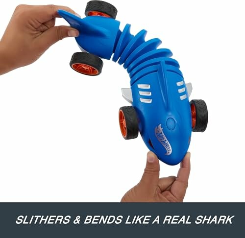 Hands holding a blue shark-shaped toy car with flexible body.