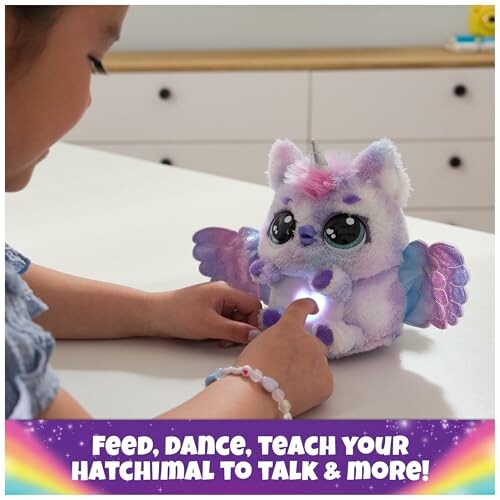 Child interacting with a colorful Hatchimal toy on a table.