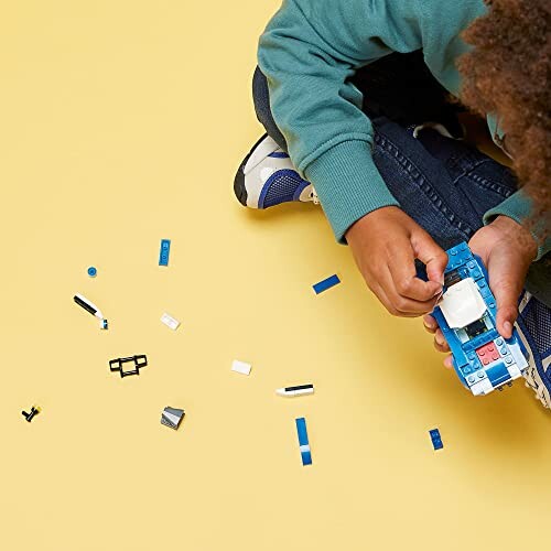 Child assembling Lego pieces on a yellow surface.