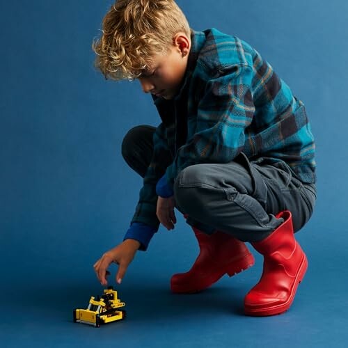 Child in red boots playing with a toy truck on a blue background.