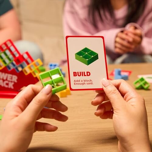 Hands holding a board game card with blocks on a table.