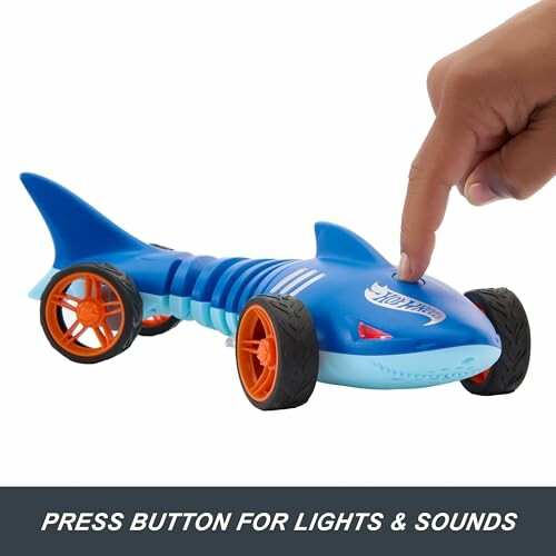 Shark-shaped toy car with orange wheels and a finger pressing a button.